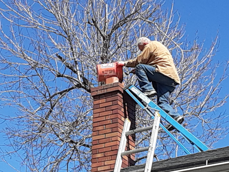 man on blue ladder on roof repairing brick chimney top