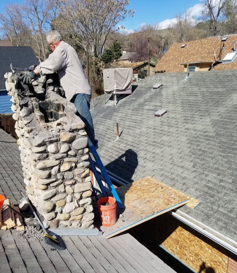 man in jeans fixing a broken chimney made out of stone
